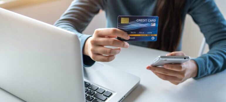 A woman holding a credit card and a mobile phone in front of a laptop.