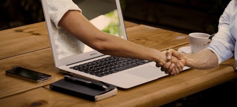 A business owner shaking hands with a customer through a laptop.