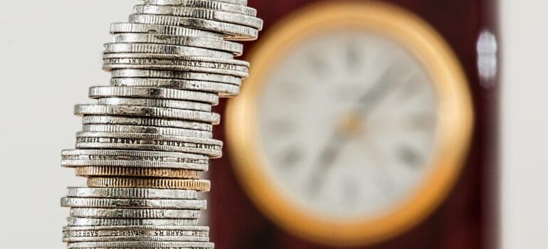 Stacked up coins with a clock in the background.