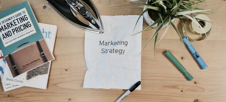 "Marketing Strategy" written on a piece of paper next to a book about marketing.