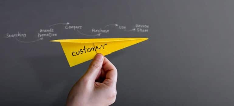 Person holding a paper plane with the customer journey written out on a blackboard in behind it.