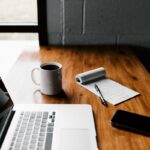 Laptop, coffee mug, notepad, and smartphone on table | The importance of nurturing a blog for your business