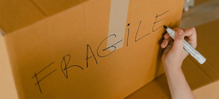 A close-up of a person writing “fragile” on the side of a moving box with a sharpie.
