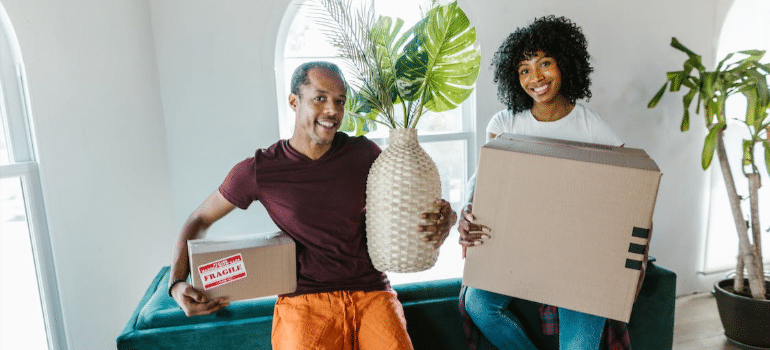 A happy couple holding plants and moving boxes in their new home.