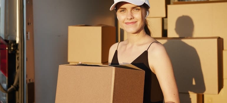 A woman holding a moving box decisive to use moving software for minimizing overhead costs