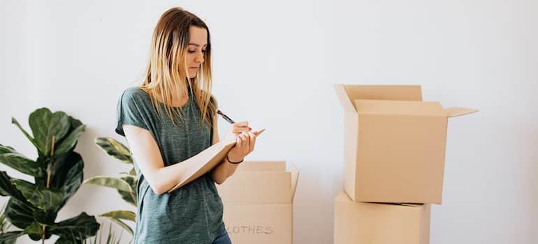 A girl standing next to moving boxes and making notes